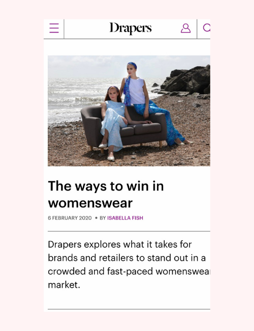 Two women sat on sofa on a sandy beach photographed for a Drapers article