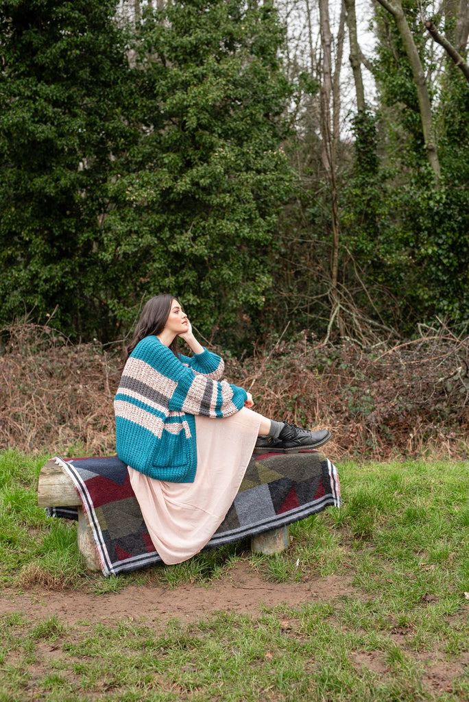 Woman sitting on wooden bench, wearing a the Allie teal and cream stripe cardigan