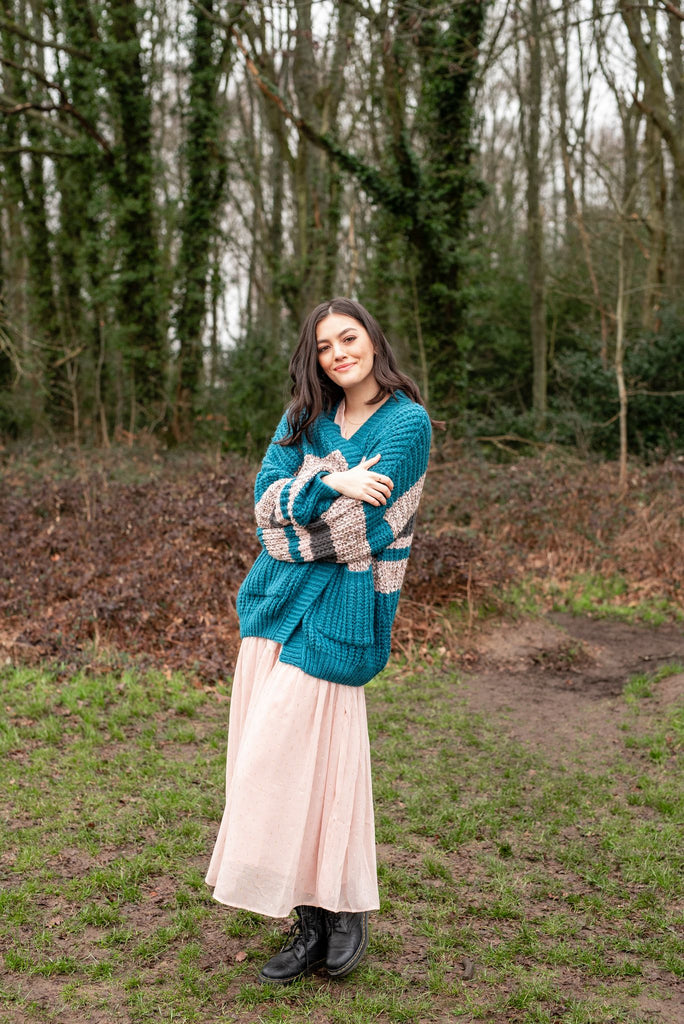 Full length photo of a smiling woman standing in woodland wearing a teal and beige cardigan