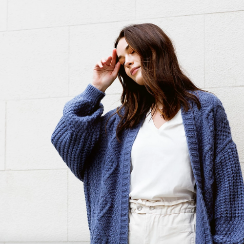 Portrait photo of a woman with closed eyes in front of a white wall wearing a navy blue long cardigan