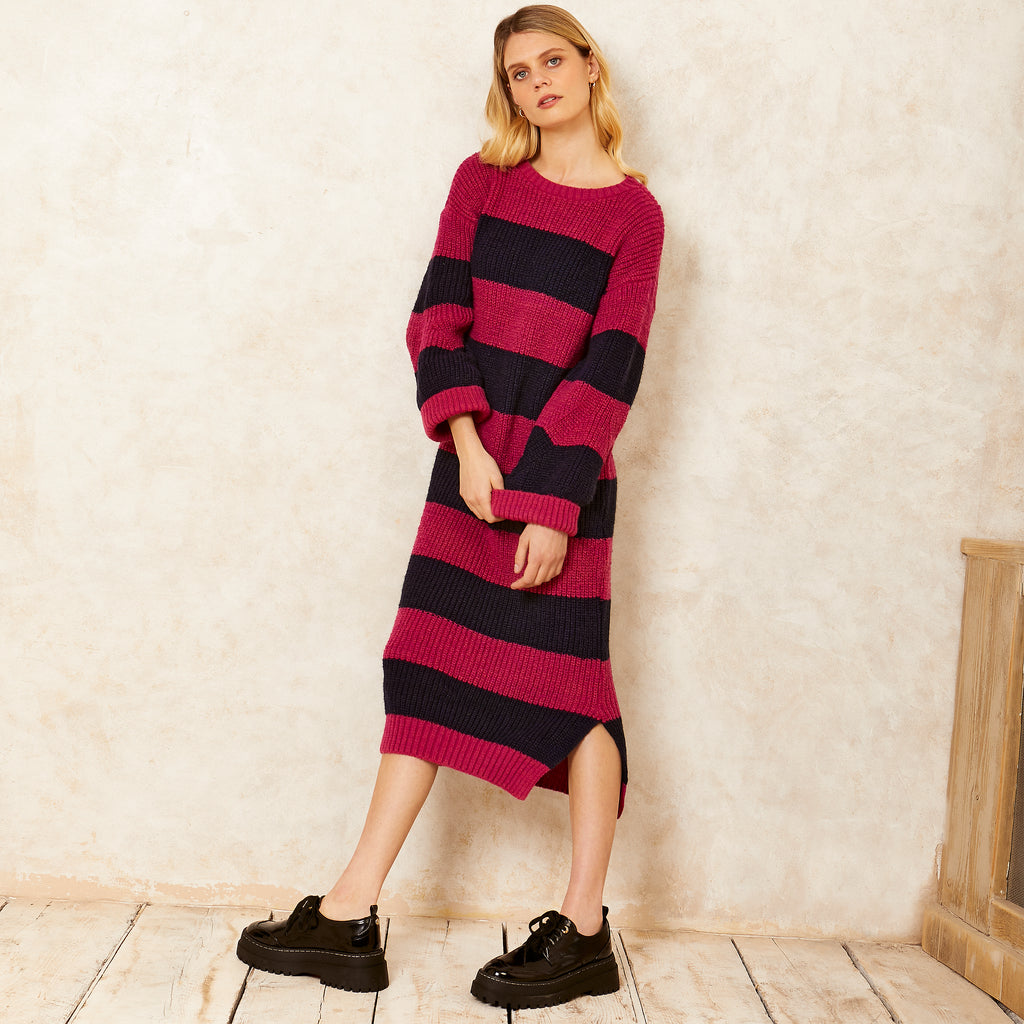 Full portrait photo of a woman in a room with bare floor boards, wearing the Antonia navy and pink stripe long knitted dress