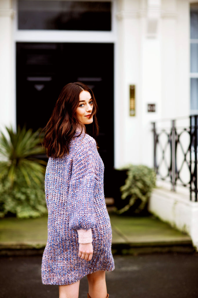 Smiling woman walking away, head turned toward camera, wearing a lilac knitted cardigan