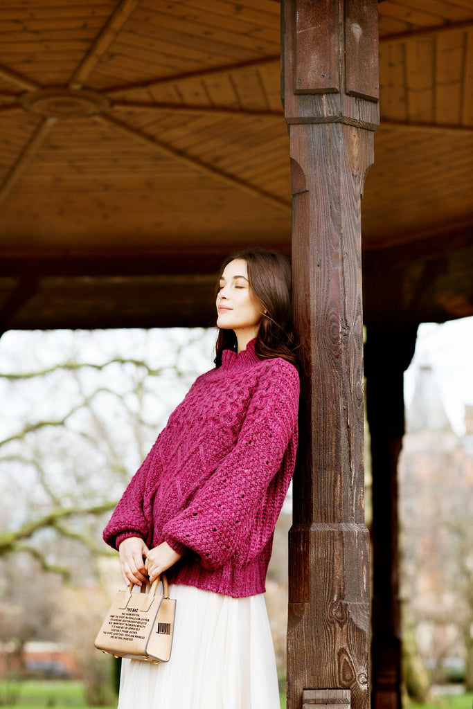 Woman under a pagoda with eyes closed, wearing a berry coloured knitted jumper