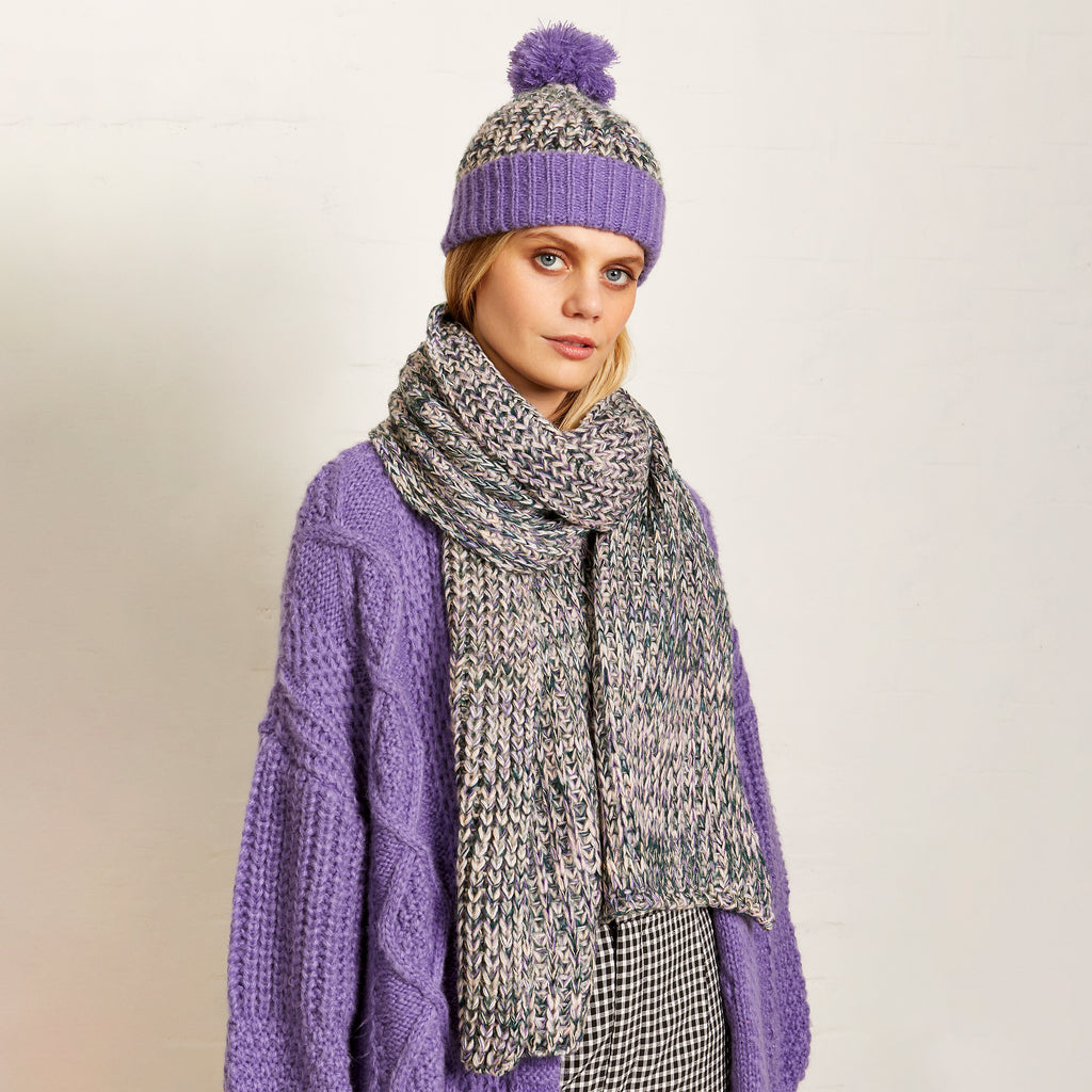Woman wearing a lilac knitted cardigan with a green and lilac hat and matching scarf