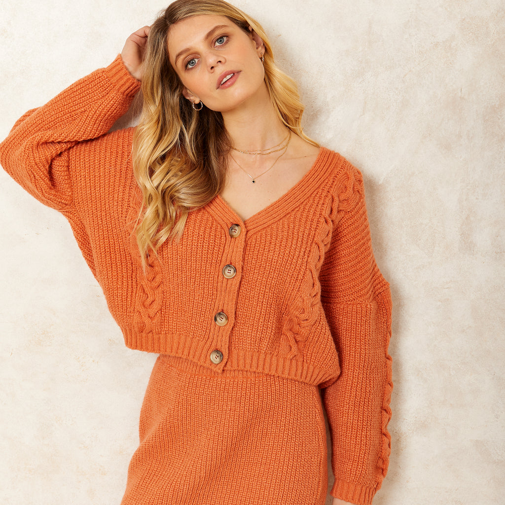 Woman stood wearing the Sienna v neck knitted orange cardigan with matching knitted skirt