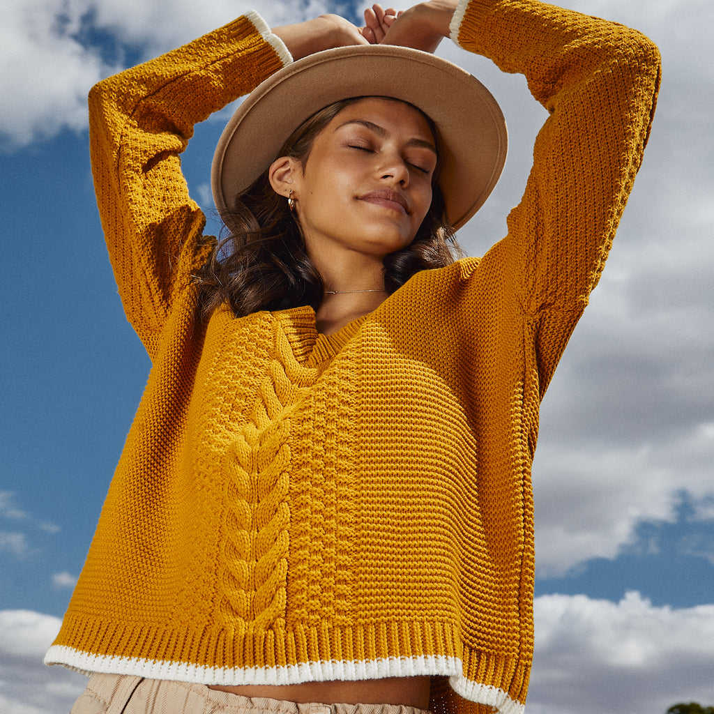 Woman with blue sky background wearing a yellow knitted jumper
